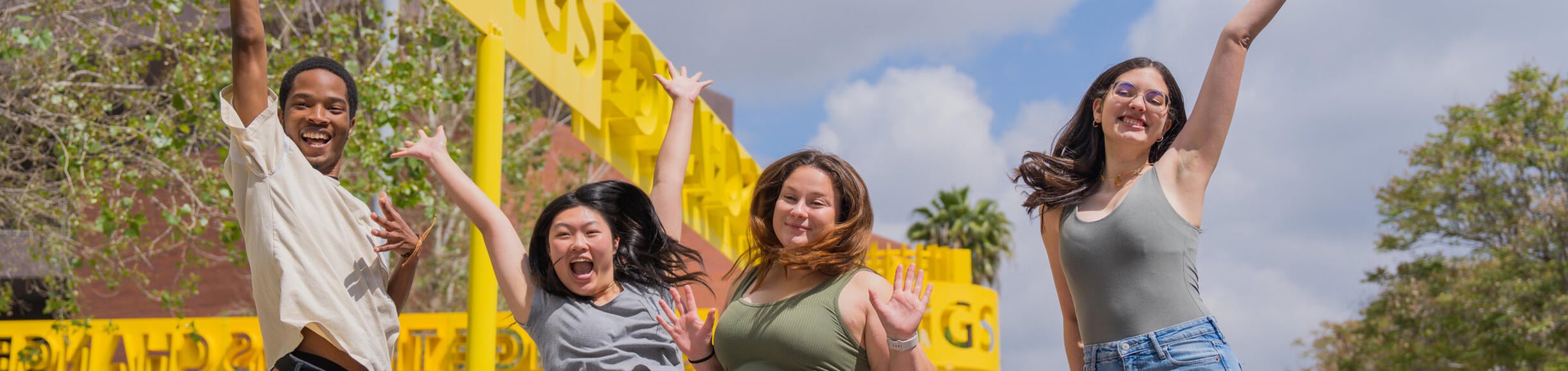 UC Riverside students jumping and smiling in front of the Change Things sculpture by the ARTS Building