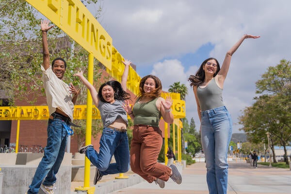 UC Riverside students jumping and smiling in front of the Change Things sculpture by the ARTS Building